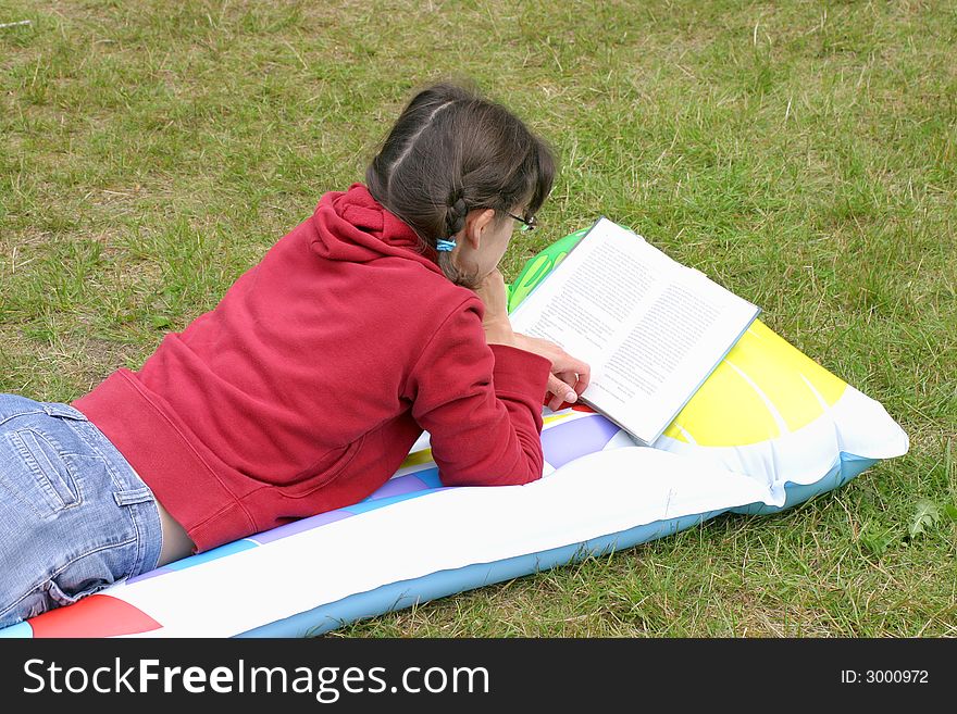 Young woman lying on the lilo and reading a book