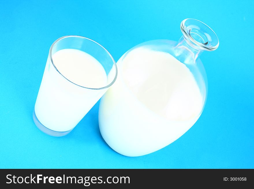Pouring white milk against blue background and glass