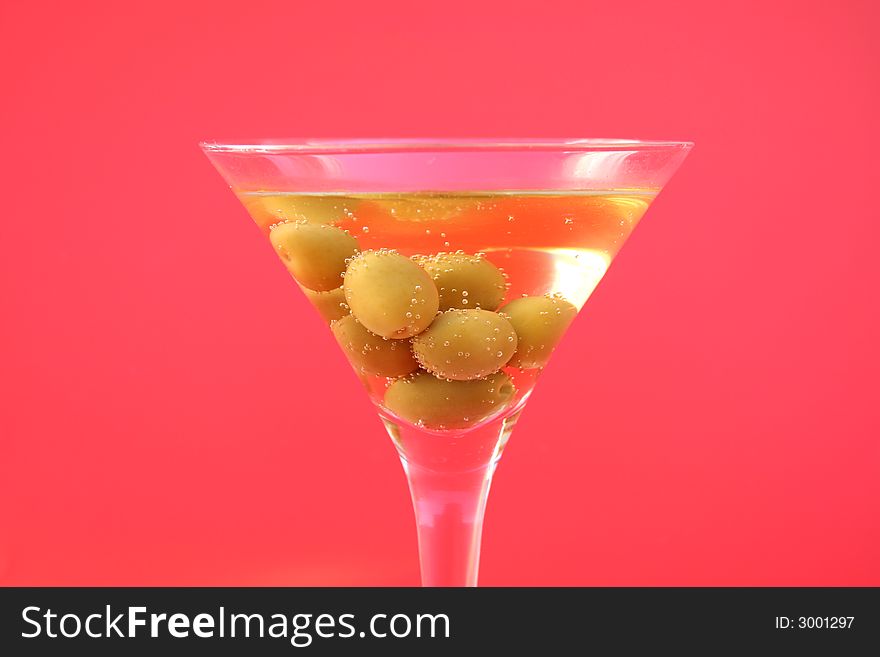 Olive cocktail in a martini glass on a red background. Olive cocktail in a martini glass on a red background