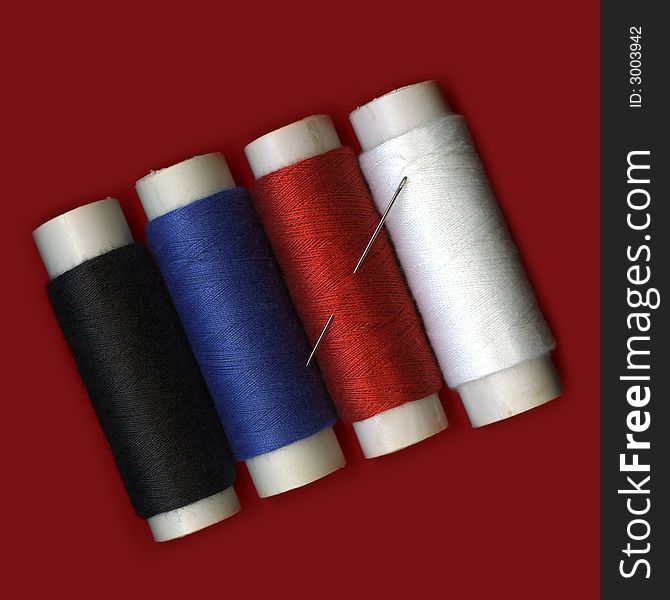 Fourth colorful spools of thread with a needle on red background