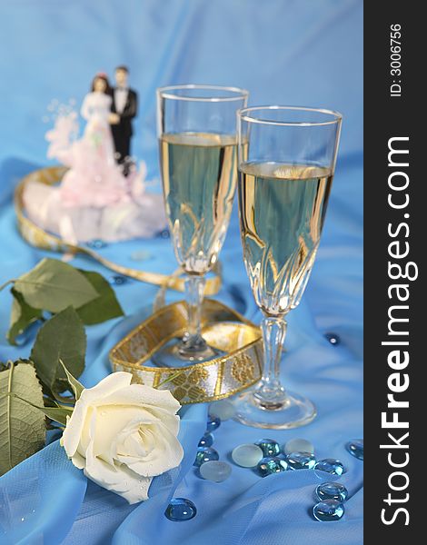 A photo of wedding cake dolls, rose and glasses over blue