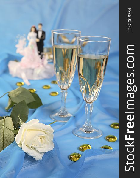A photo of wedding cake dolls, rose and glasses over blue