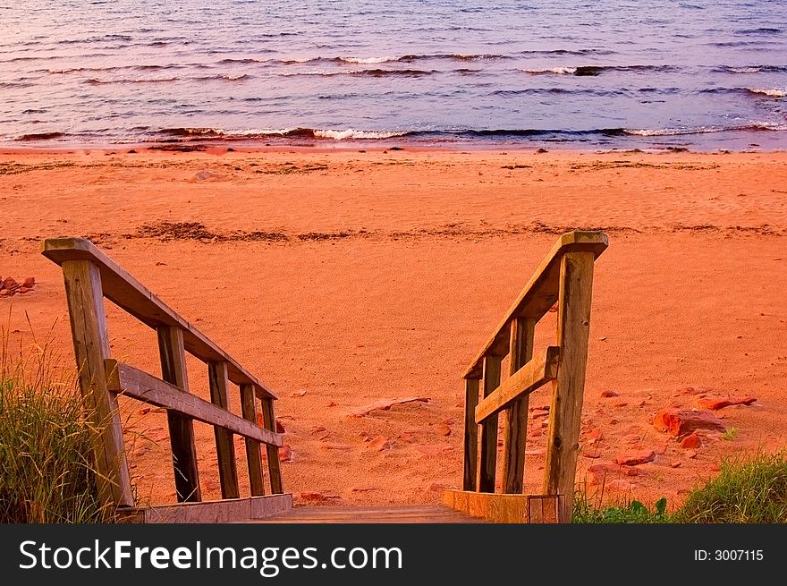 A flight of wooden stairs descending to a red sandy beach in sunset light.