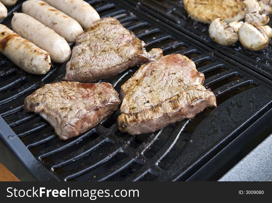A selection of meats on a gas barbecue, focusing on steak & sausages