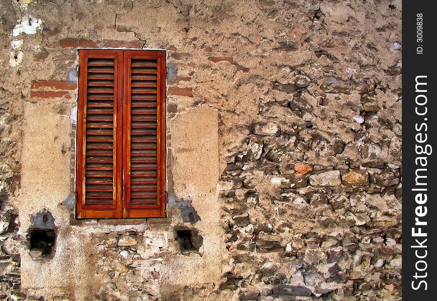 Old window with closed shutters and decayed stone wall