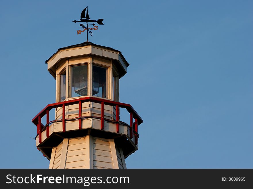 Old light house with weather vane silhouetted against a blue sky