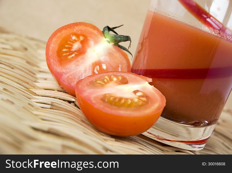 Half of fresh tomato put beside a glass of tomato juice