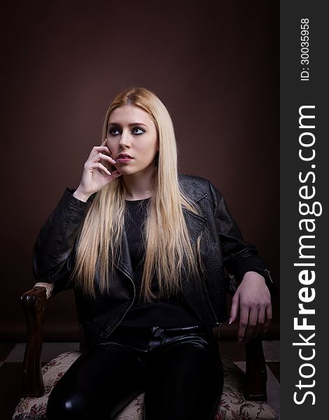 Gorgeous caucasian girl sitting on a vintage chair in leather jacket studio shot