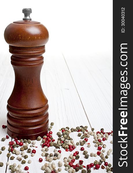 Pepper-mill with peppercorns on white background