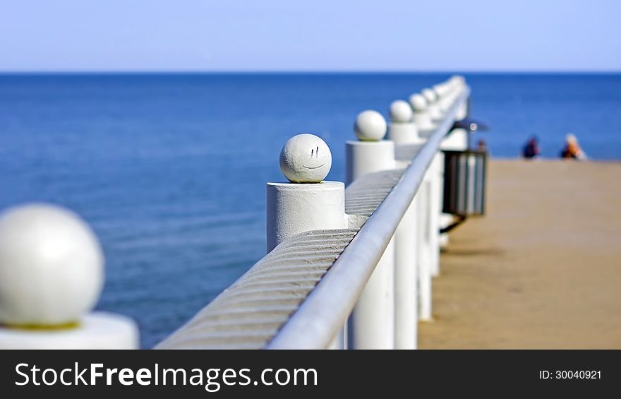 Sea pier railing with a painted smiley. Against the background of the sea horizon.