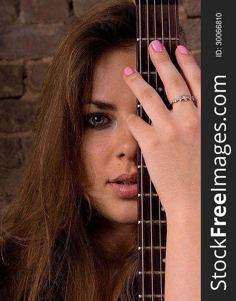 Portrait of a Girl. In the foreground, neck of the guitar. In the background a brick wall. Portrait of a Girl. In the foreground, neck of the guitar. In the background a brick wall