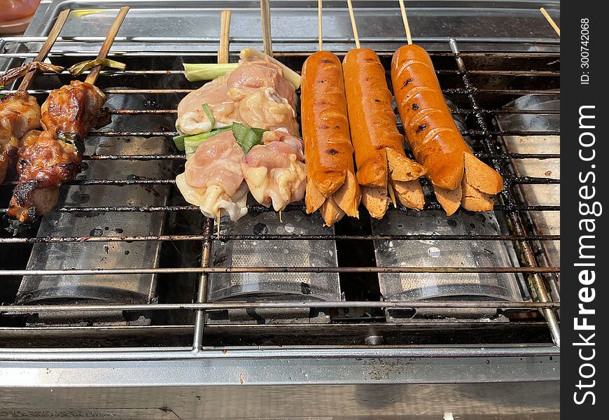 Sausages and meat on skewers are on the iron grill of the satay grill