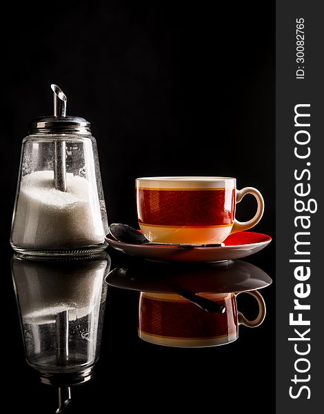 Sugar-basin with white sugar and a cup of tea or coffee on reflecting surface. on black. Shot in studio. Sugar-basin with white sugar and a cup of tea or coffee on reflecting surface. on black. Shot in studio