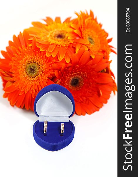Two gold wedding rings in the blue box with a bouquet of orange gerberas. Two gold wedding rings in the blue box with a bouquet of orange gerberas