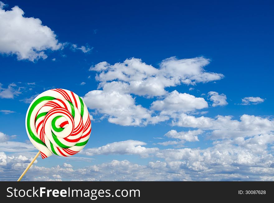 Single lollipop in white green and red on background of sky and clouds. Single lollipop in white green and red on background of sky and clouds