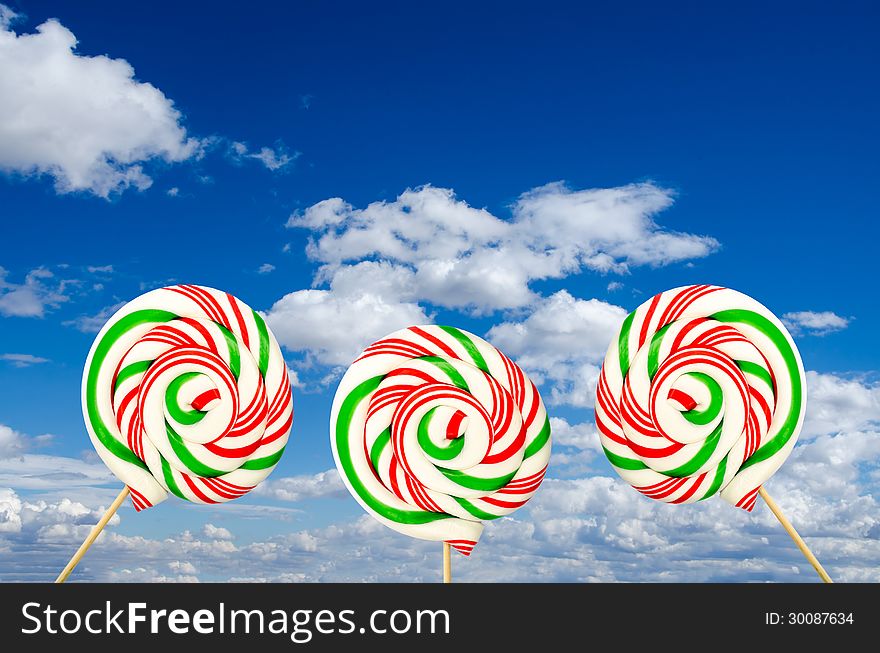 Sugar lollipops in white green and red on background of sky and clouds. Sugar lollipops in white green and red on background of sky and clouds