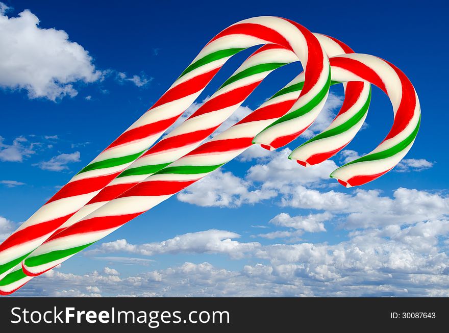 Sugar sticks in white green and red on background of sky and clouds. Sugar sticks in white green and red on background of sky and clouds