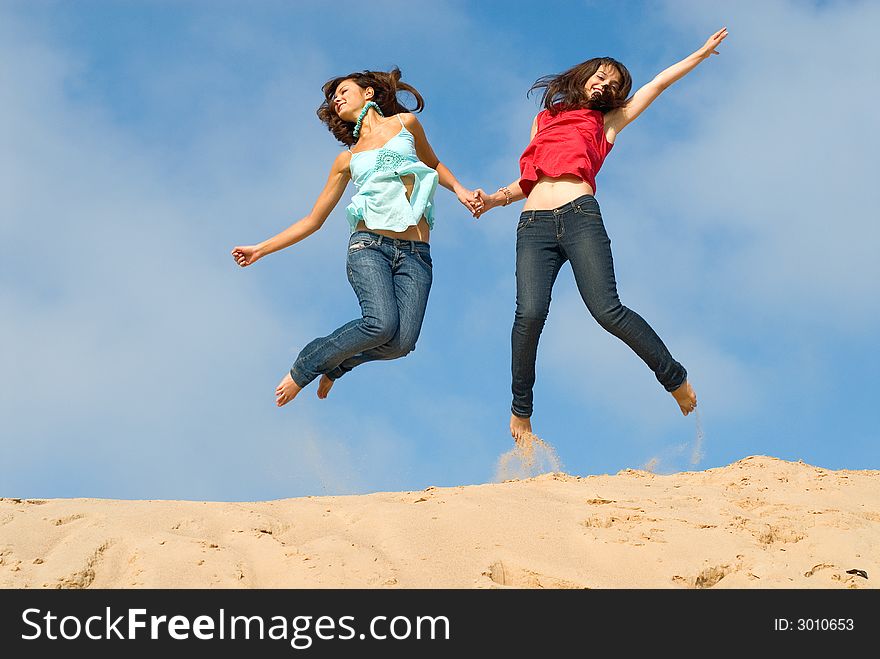 Two girlfriends jump with happiness on sand. Two girlfriends jump with happiness on sand