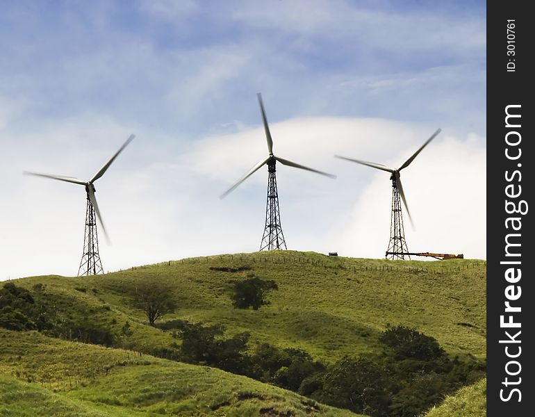 Three windmills harvesting power on a green hilltop. Three windmills harvesting power on a green hilltop.