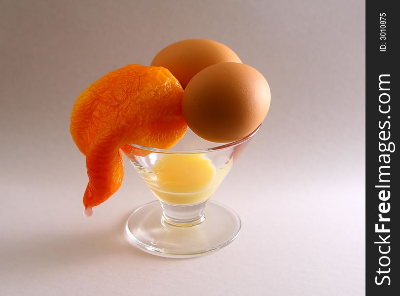 Flabby orange pepper and two eggs in a cocktail glass on a light grey background