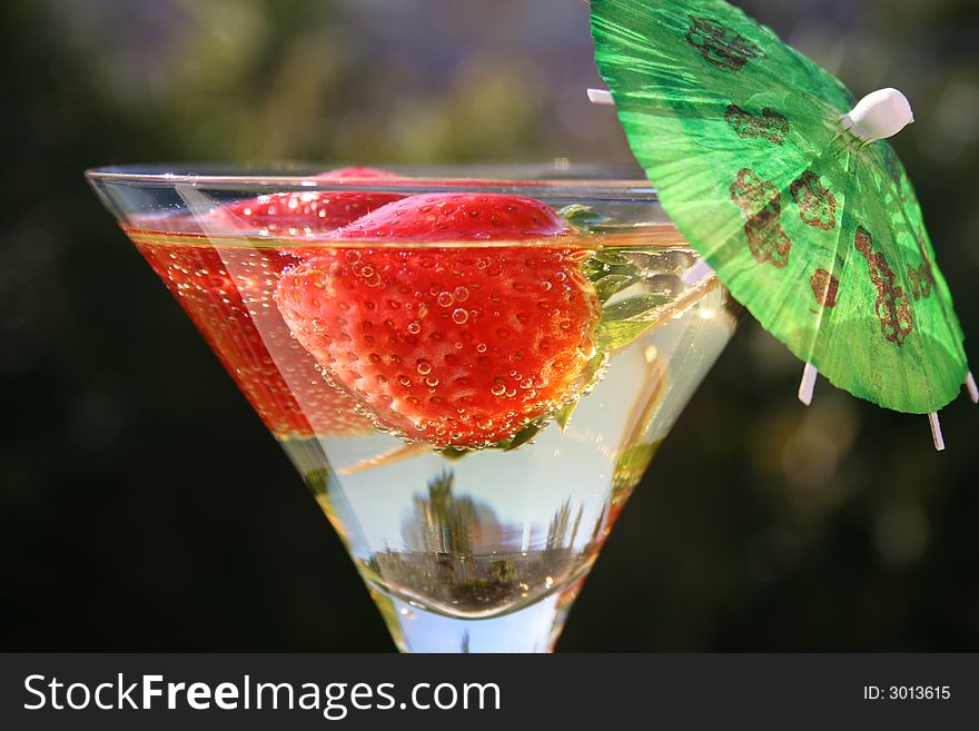 Strawberries in a martini glass with an umbrella in the sun. Strawberries in a martini glass with an umbrella in the sun