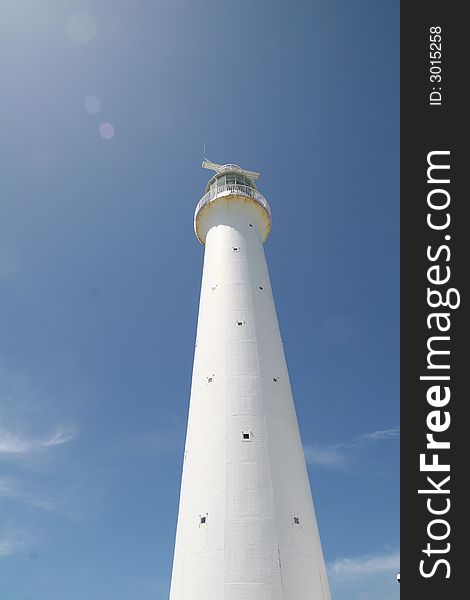 A white lighthouse rising into the blue sky against the sun. A white lighthouse rising into the blue sky against the sun