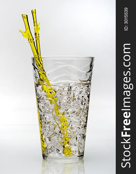 Cold drink with ice and yellow stirring rod isolated on white background