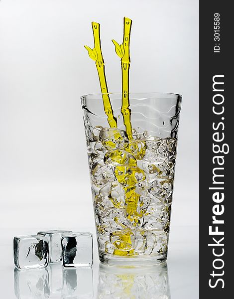 Cold drink with ice and yellow stirring rod isolated on white background