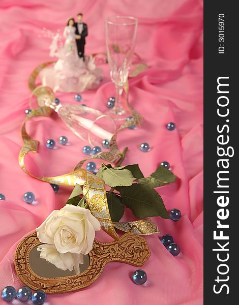 A photo of wedding cake dolls, rose and glasses over pink