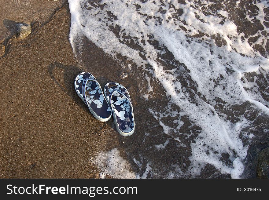 Light blue sandals on sand at beach, water washing up