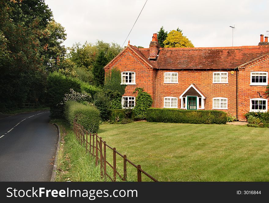 Quaint red brick English Rural Cottage and garden with an iron fence bordering the lawn