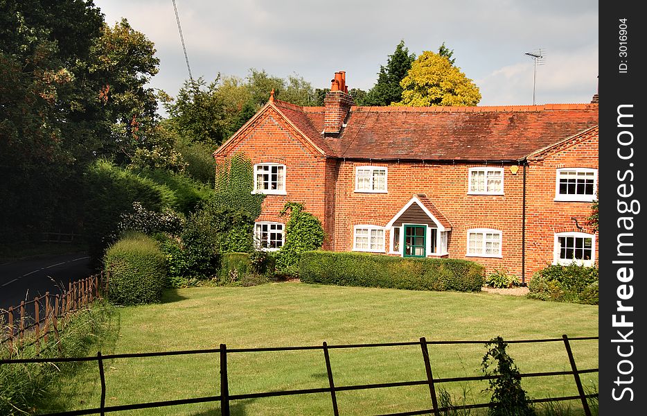 Quaint red brick English Rural Cottage and garden with an iron fence bordering the lawn