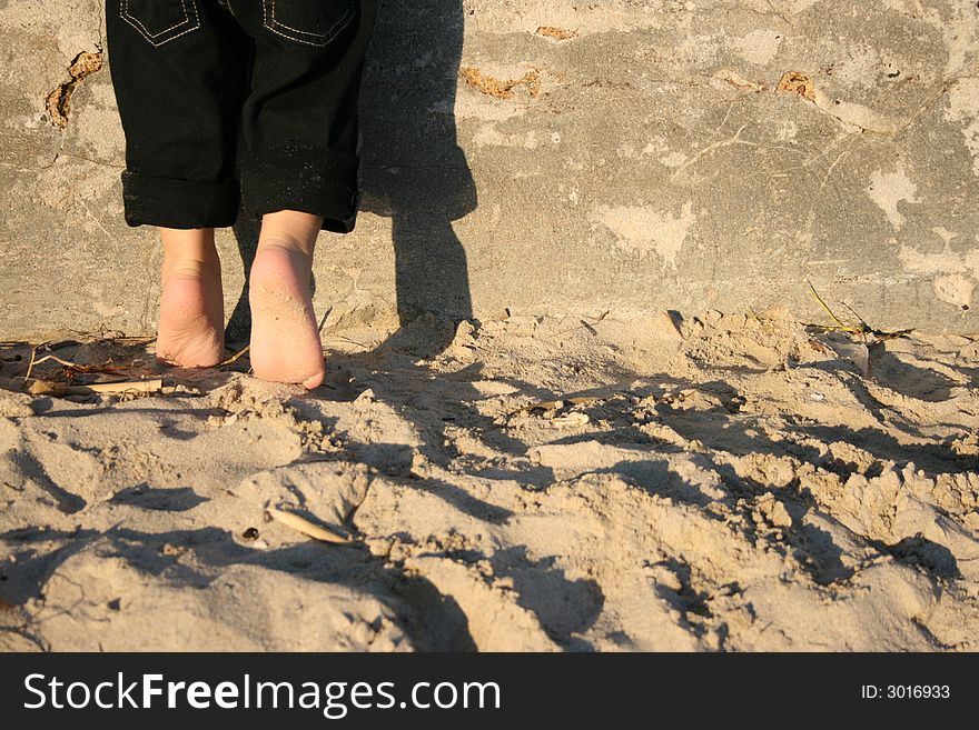Toddler standing on the beach against a wall on his tippie toes