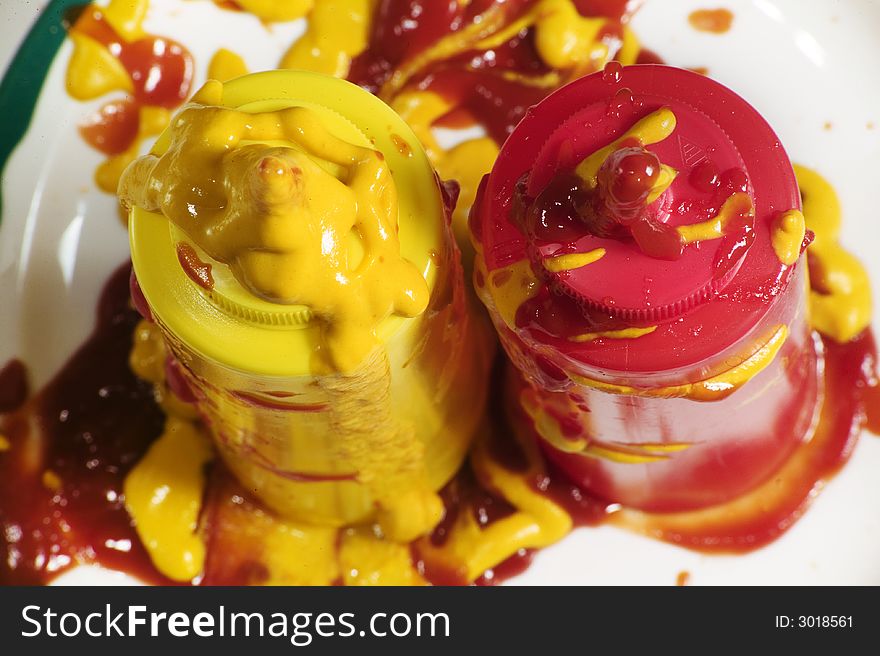 Messy mustard and ketchup squeeze bottles standing up on a plate.