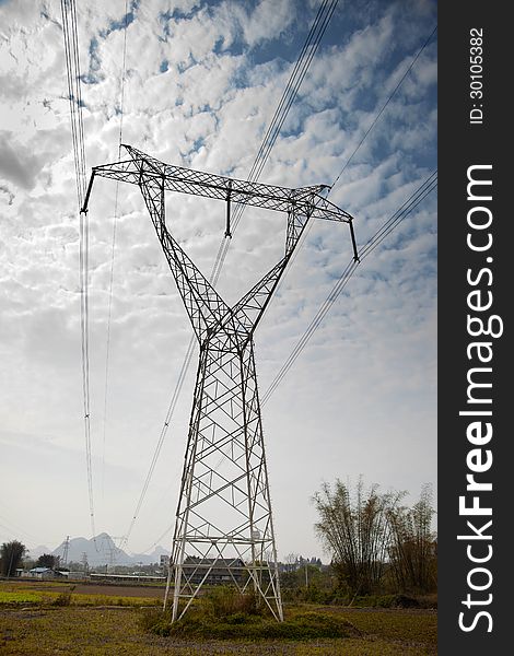 A high voltage power tower with cloudy sky in cropland