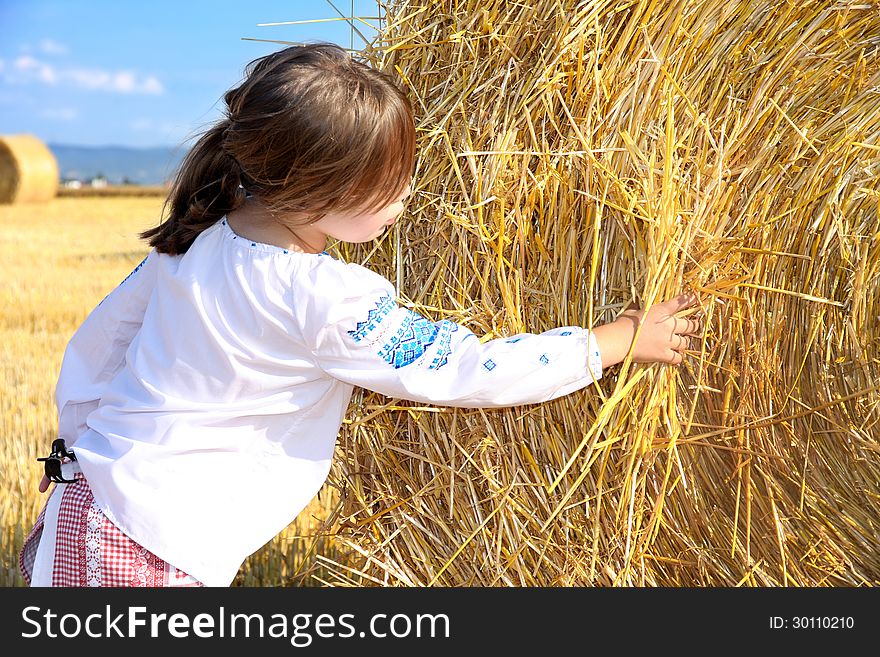 Small rural girl on harvest field with straw bales