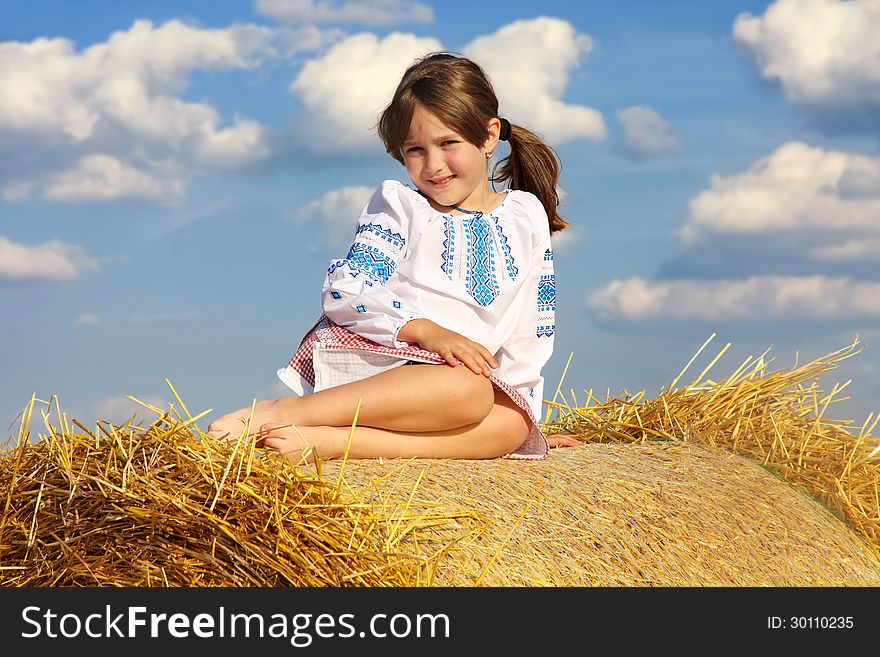 Small rural girl on the straw after harvest field with straw bales