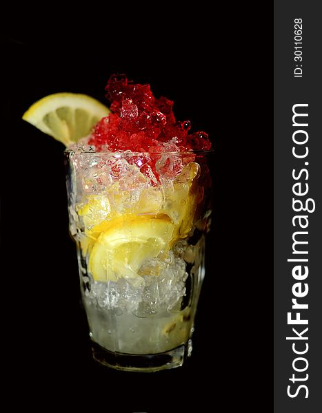 A drink in tall glass with lemon and ice, and red garnish