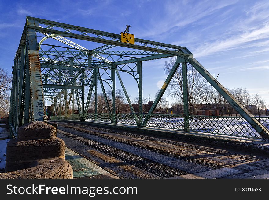 Small steel bridge crossing the canal with winter scenery in the background