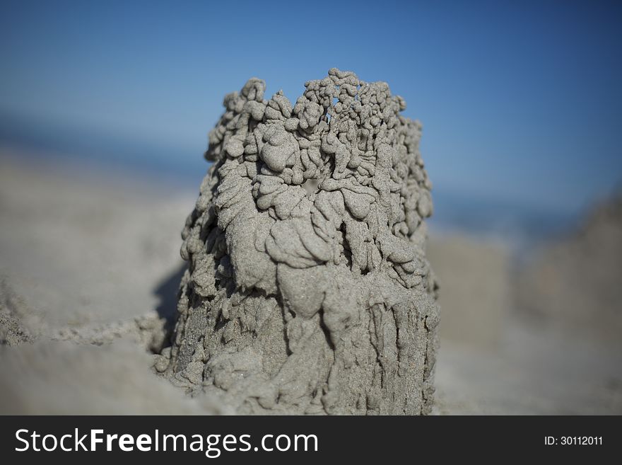 Close up of a sand castle made from dribbled sand. Blue sky in background.