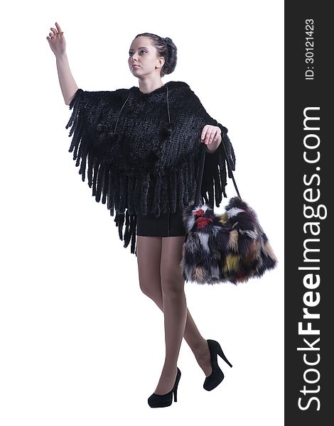 Beautiful face brunette model walking and looking up, showing hand gesture. She is wearing fancy black woolen poncho, short skirt and high-heel shoes, and having a colorful fur bag. Isolated on white background. Shot in studio. Beautiful face brunette model walking and looking up, showing hand gesture. She is wearing fancy black woolen poncho, short skirt and high-heel shoes, and having a colorful fur bag. Isolated on white background. Shot in studio.