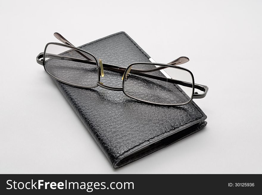 Black notepad on a white background and glasses. Black notepad on a white background and glasses