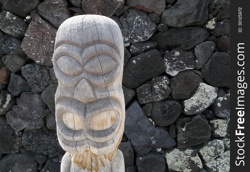 Face of a carved wood tiki statue standing in front of a lava rock wall at Puuhonua O Honaunau Place of Refuge historical park on the big island of Hawaii. Face of a carved wood tiki statue standing in front of a lava rock wall at Puuhonua O Honaunau Place of Refuge historical park on the big island of Hawaii.