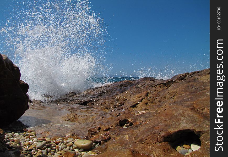Gravel, wet, rocky coast and splashing waves against clear, blue sky in a sunny day, Thassos Island, Greece. Gravel, wet, rocky coast and splashing waves against clear, blue sky in a sunny day, Thassos Island, Greece