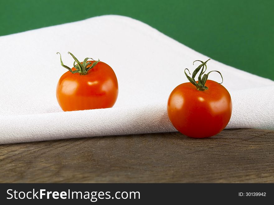 Ripe tomatoes and a napkin on a wooden table, green background