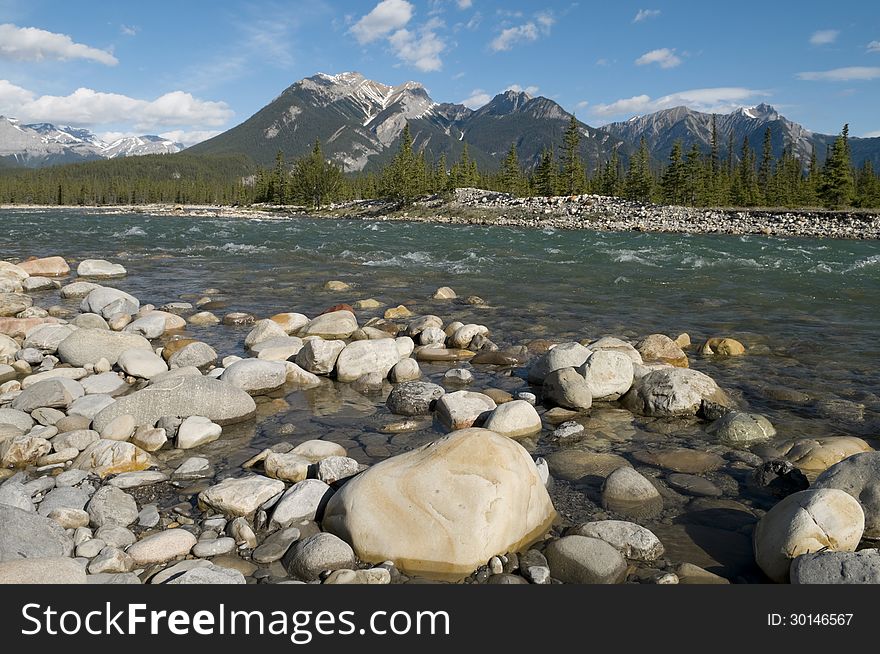 Selective focus on the rocks in the foreground with mountains in the background at Snaring River located in Jasper National Park, Alberta, Canada. Selective focus on the rocks in the foreground with mountains in the background at Snaring River located in Jasper National Park, Alberta, Canada.