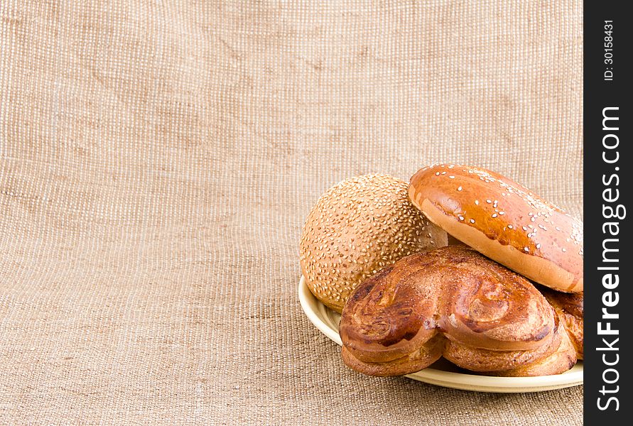 Bread rolls with sesame seeds on a plate on the background of sacking