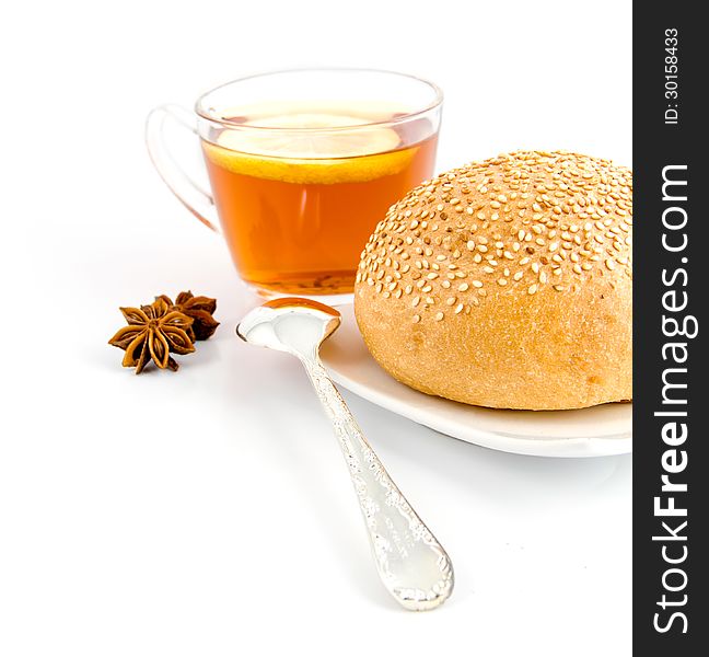 Roll with sesame,tea spoon and anise on the background of tea with lemon in a clear plastic Cup on the white. Roll with sesame,tea spoon and anise on the background of tea with lemon in a clear plastic Cup on the white