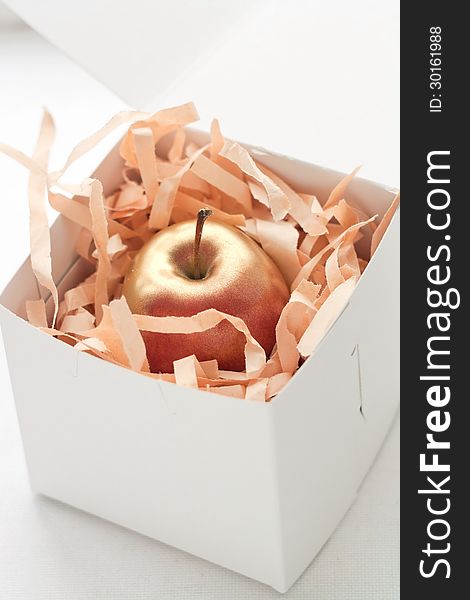 An apple painted in gold in a white gift box. An apple painted in gold in a white gift box