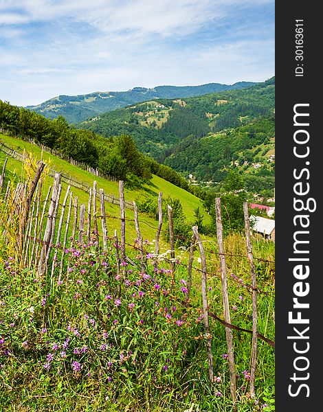 Wooden stick fence in village in mountains with blue sky, green grass and path in good weather time. Wooden stick fence in village in mountains with blue sky, green grass and path in good weather time